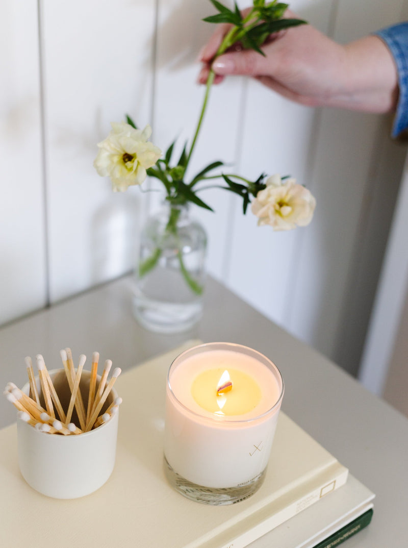 candle with wood wick burning styled on top of books with flowers in the background